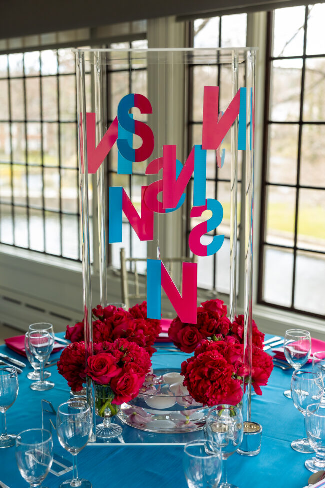 Close-up of floral centerpiece on acrylic stand with colorful floating initials